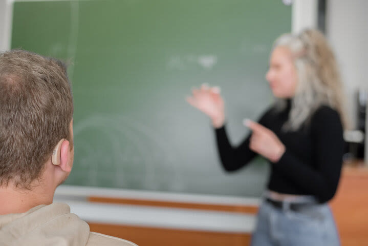 Estudiante universitaria comunicándose en señas frente a la pizarra